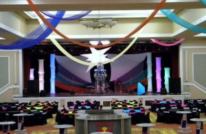 Colorful ceiling swags hang from the ceiling, lit towers set the stage, and colorful chair bands bring this event together