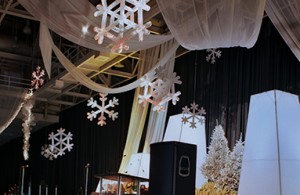 Metal snowflakes, white chiffon, and white towers decorate the stage for a corporate holiday event.