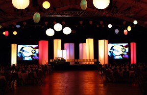 Lighted towers and Chinese Lanterns decorate the stage for a corporate event.